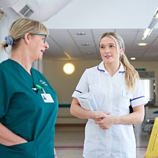 Woman in the centre of the frame, in a healthcare support worker uniform, speaking to colleagues